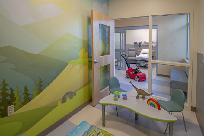 A waiting room inside a medical office for pediatric patients with toys on a table and a nature scene on the wall
