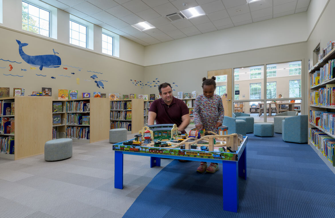 Children's room with book stacks with parent and child using activity table at North Hampton Public Library